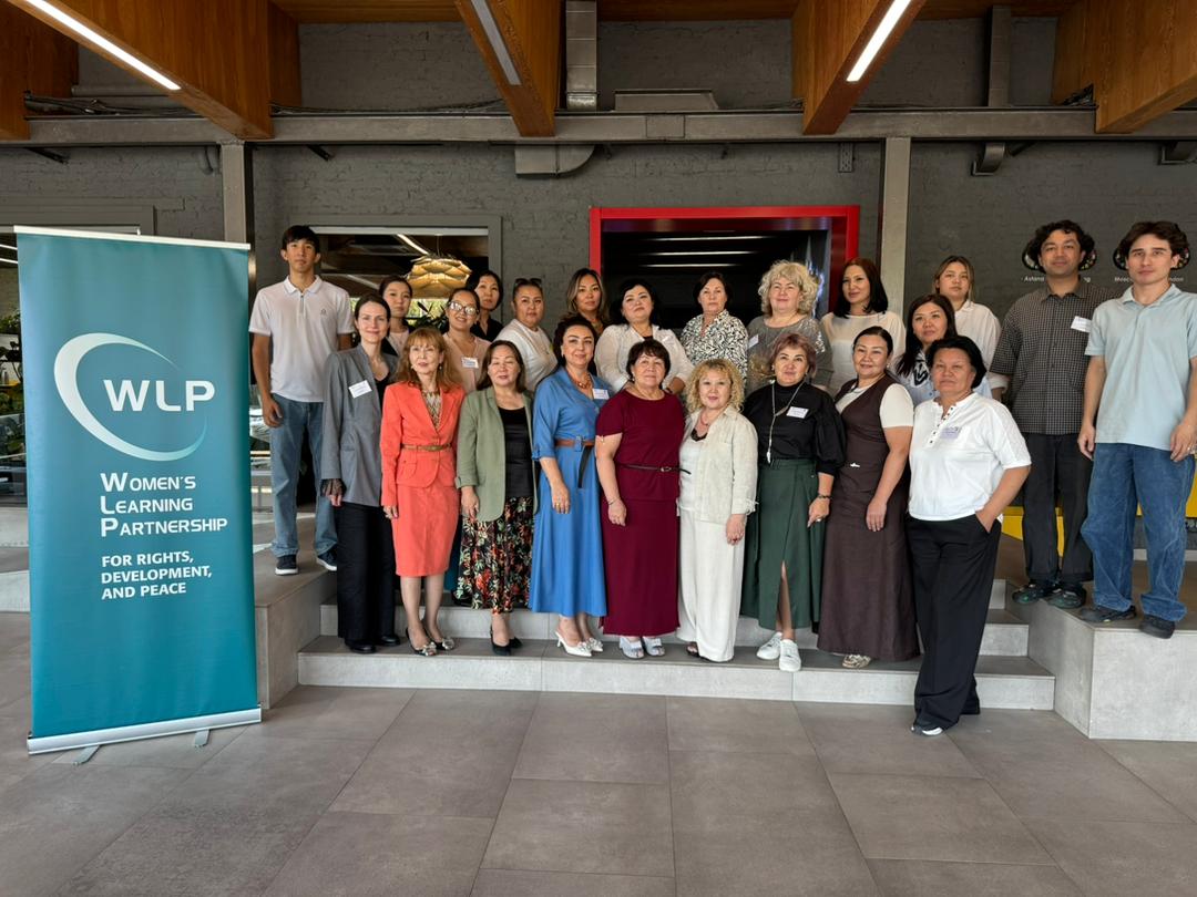 A large group of women from central Asia standing besides a WLP sign